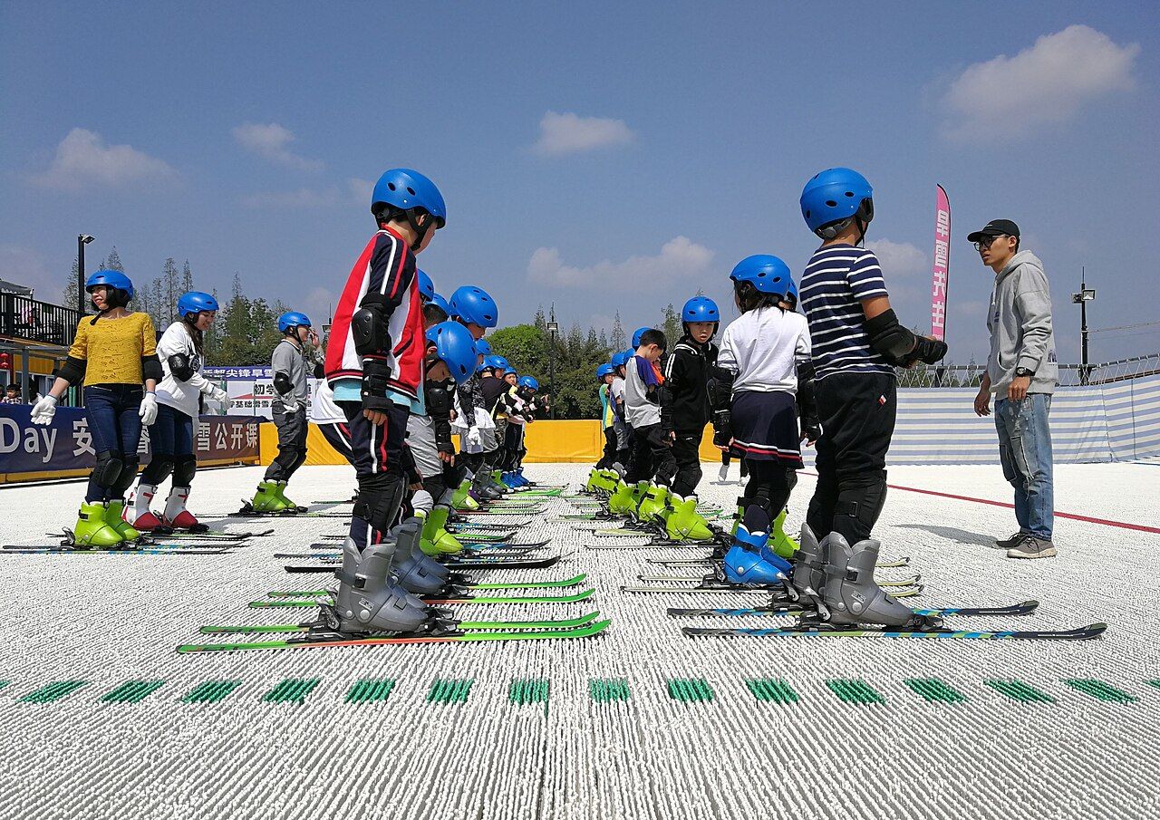 Kids in helmets lined up on skis during a group ski lesson