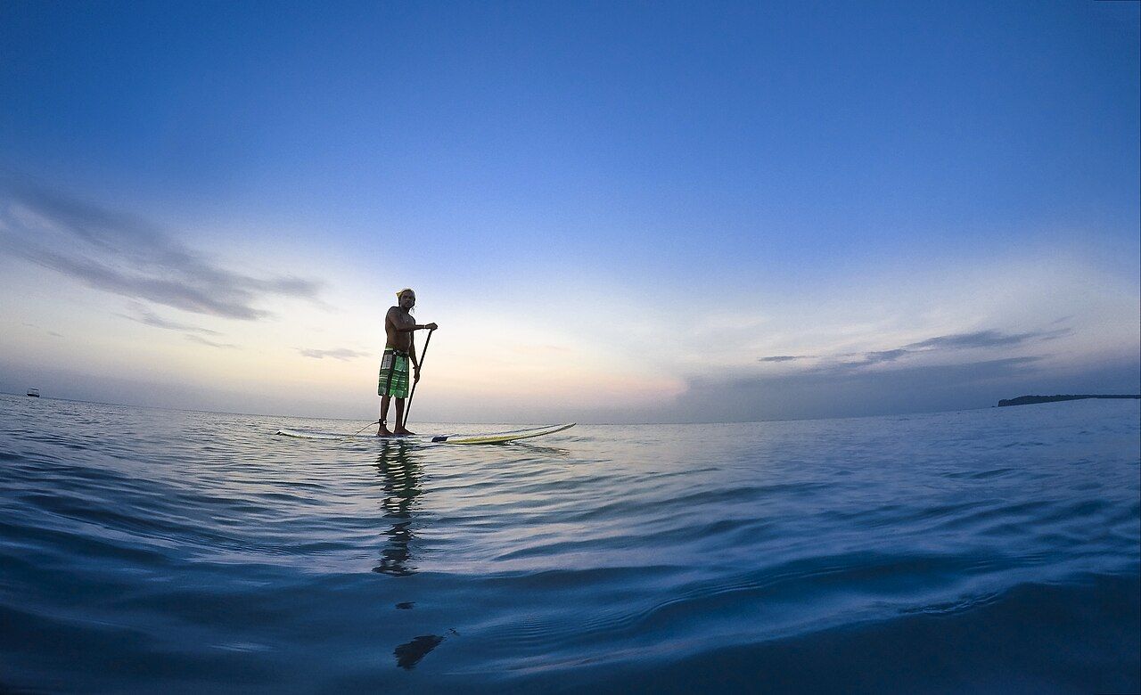 Stand-up paddleboarder on calm open water at dusk